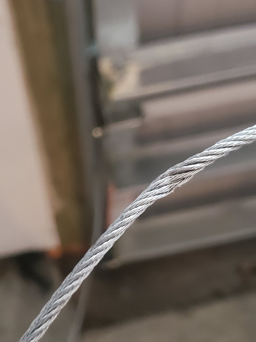 Frayed garage door lift cable wrapping around a cable drum — an early post-storm warning sign